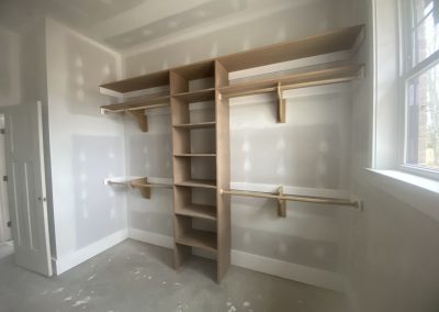 Unfinished walk-in closet with wooden shelves, hanging rods, and a window letting in natural light.