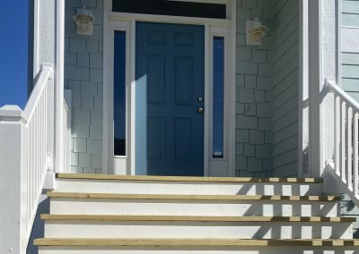 A blue front door with side windows at the top of white-painted wooden steps and railings.