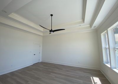 Bright, empty room with light wood floors, large windows, and a modern black ceiling fan.