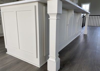 White kitchen island with decorative trim and support post, set on dark wood flooring.