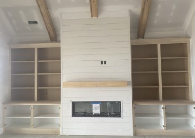 Modern living room with a central fireplace, wooden beams, and built-in shelves and cabinets on both sides.