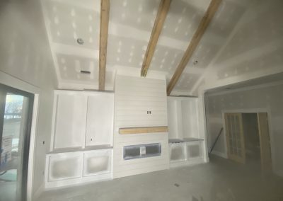 Unfinished living room with exposed beams, built-in cabinets, and a shiplap fireplace under construction.