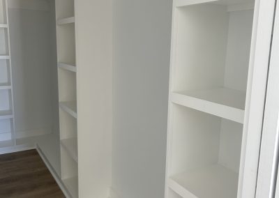 White built-in shelves and open closet space in a room with wood flooring.