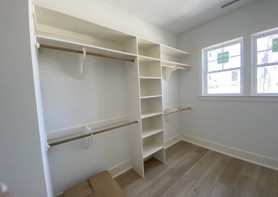 Empty walk-in closet with shelves, hanging rods, and a cardboard box on the wood floor near two windows.