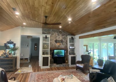 A cozy living room with a stone fireplace, wooden ceiling, and large window letting in natural light.