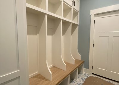 White built-in mudroom lockers with wood bench, cubbies, and blue patterned tile floor.