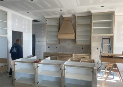 A person stands in a kitchen under construction with unfinished cabinets and open shelves.