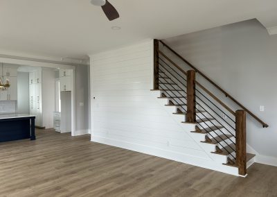 Modern interior with wood flooring, open kitchen, and a staircase with wood and metal railing.