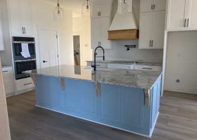 Modern kitchen with a large blue island, marble countertop, white cabinets, and wood accents.