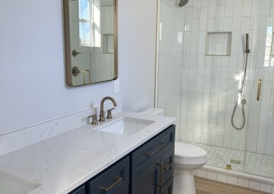 Modern bathroom with blue vanity, gold hardware, white countertop, and glass shower with gold fixtures.
