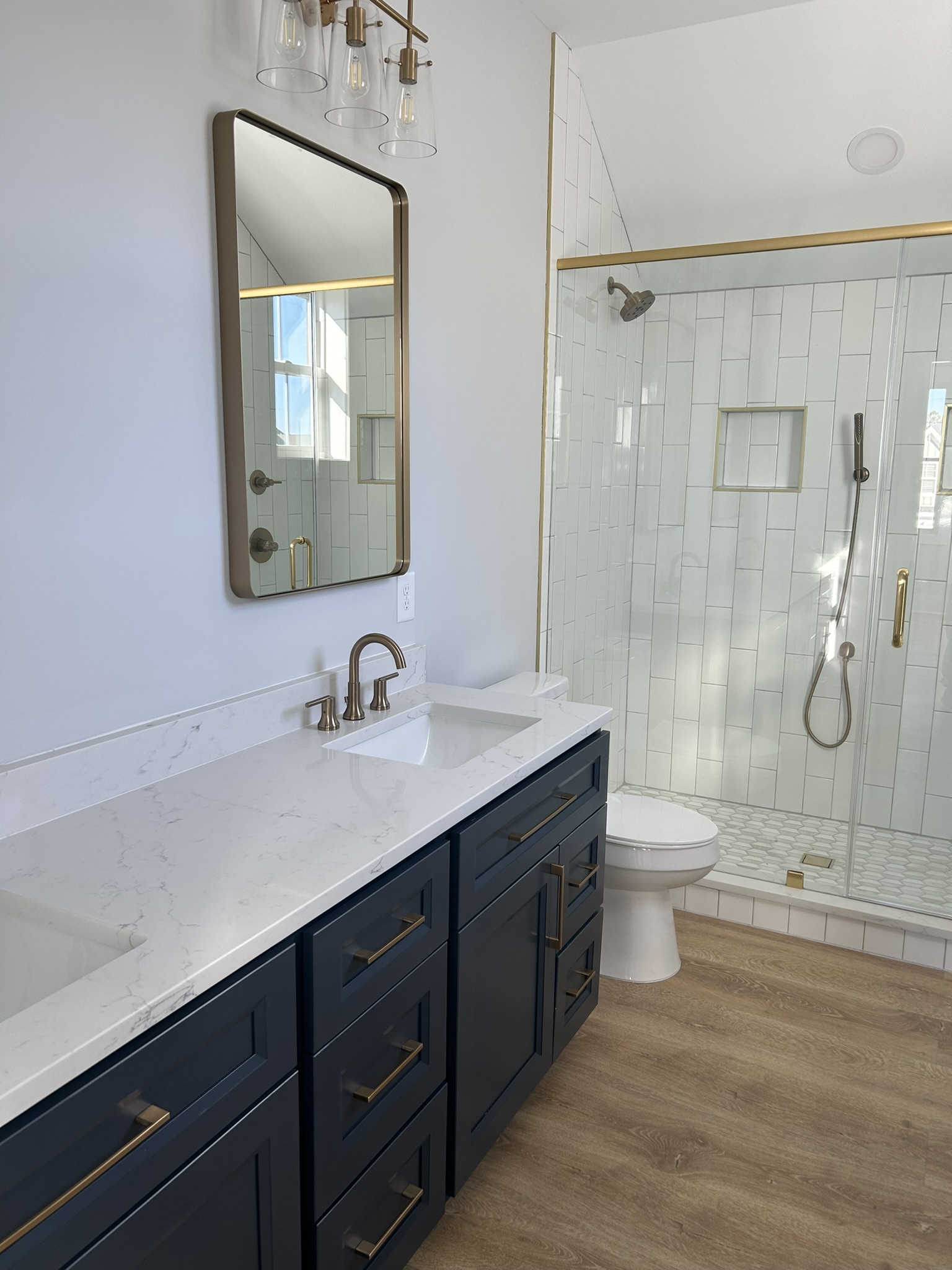 230AF989-7FE4-4B33-81AF-599D03F15B57_1_102_o Modern bathroom with blue vanity, gold hardware, white countertop, and glass shower with gold fixtures.