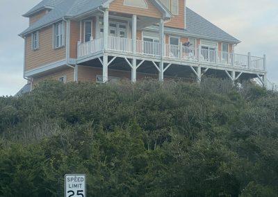 A large orange house on a hill with a wraparound porch; a speed limit 25 sign is in front.