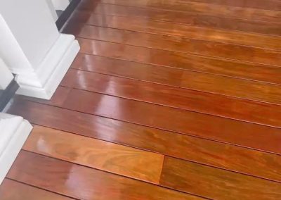 Shiny, freshly polished wooden porch floor in front of a door with white railings and columns.