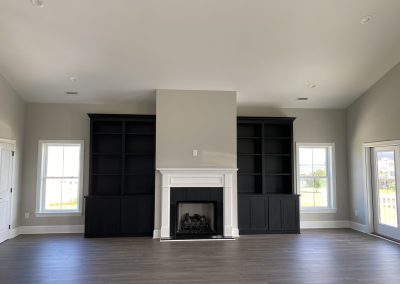 Modern living room with dark built-in shelves, a white fireplace, and large windows letting in natural light.