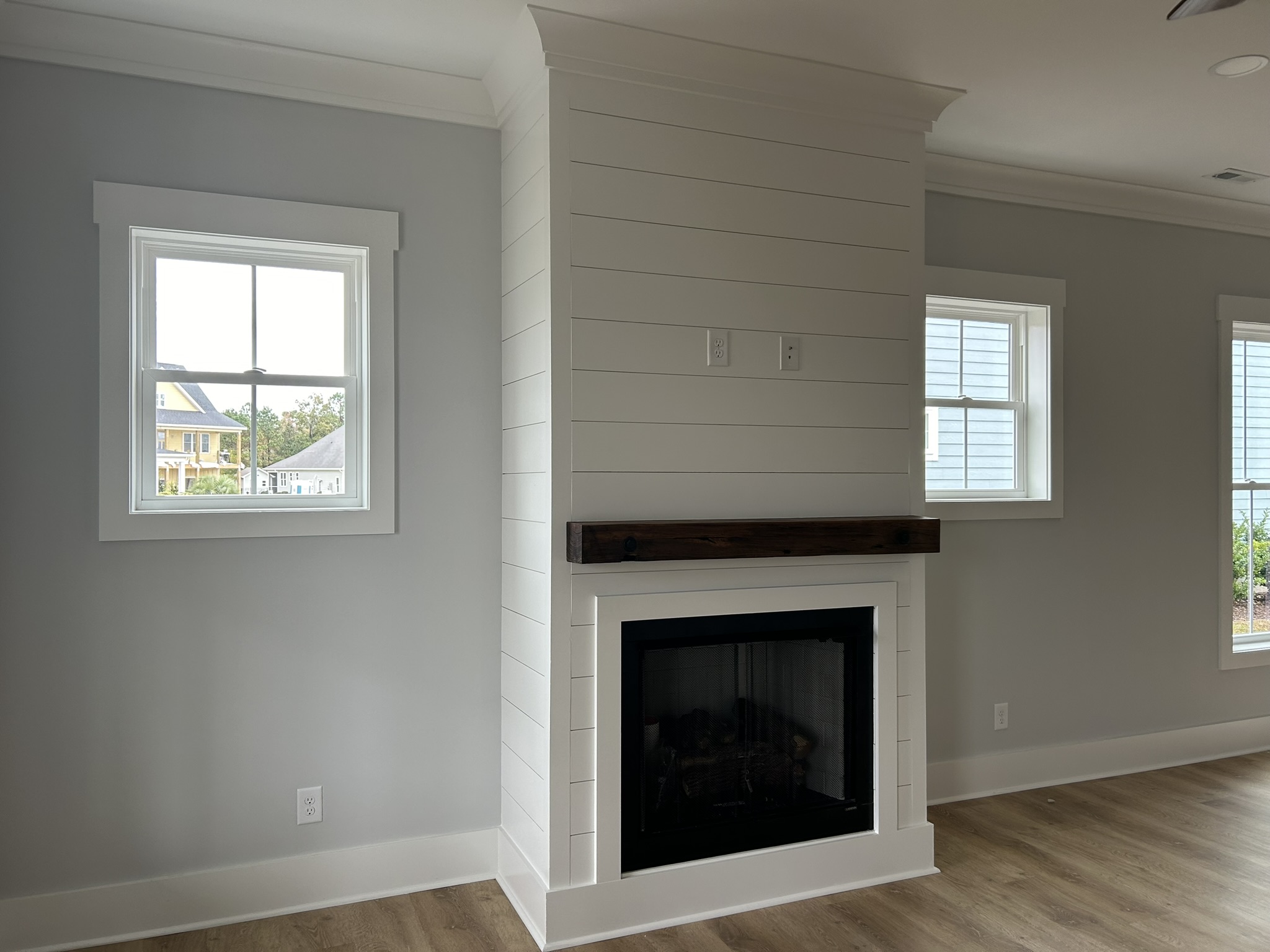 31370F0A-8806-49D6-B7C0-2455EBE32EFA_1_102_o Interior house painting: Modern living room with a central shiplap fireplace, wood mantel, and two windows on either side.
