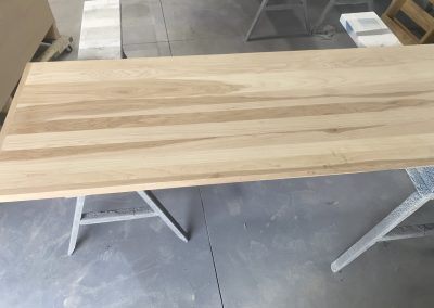 A light wood tabletop on sawhorses in a workshop with a gray concrete floor.