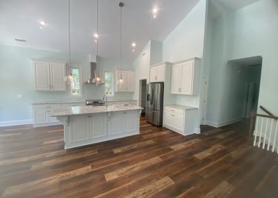 Modern kitchen with white cabinets, granite island, stainless appliances, and wood flooring.