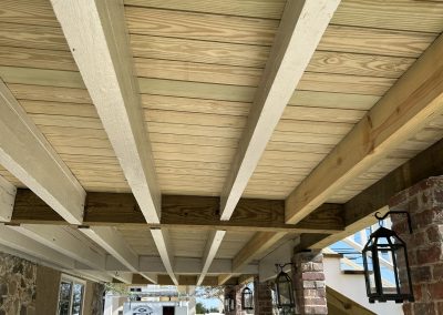 View from below a wooden porch roof with beams, brick columns, benches, and hanging lanterns.