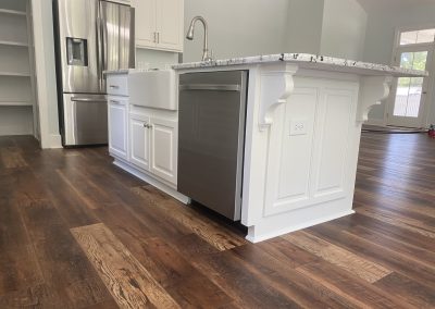 Modern kitchen with a white island, farmhouse sink, stainless appliances, and dark wood floors.
