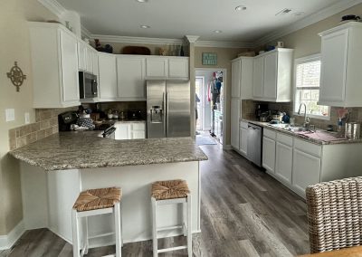 Bright kitchen with white cabinets, stainless appliances, and two stools at a marble countertop.