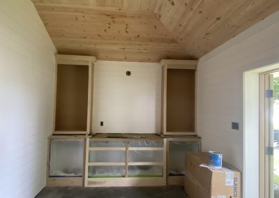 Unfinished wooden cabinets and shelving in a room with wood-paneled ceiling and white walls.