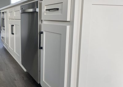 White kitchen cabinets with black handles and a stainless steel dishwasher on wood flooring.