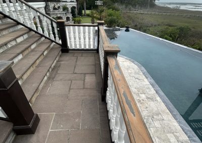 Stone patio with stairs, a pool, white railing, and a view of grassy marshland by the water.