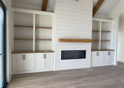 Modern living room with built-in white shelves, a fireplace, and wooden accents on the mantel and ceiling beams.