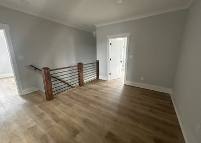 A hallway with light wood flooring, gray walls, and a staircase with a wooden railing.