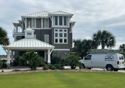 A white van is parked outside a large beach house with palm trees and a well-kept lawn.