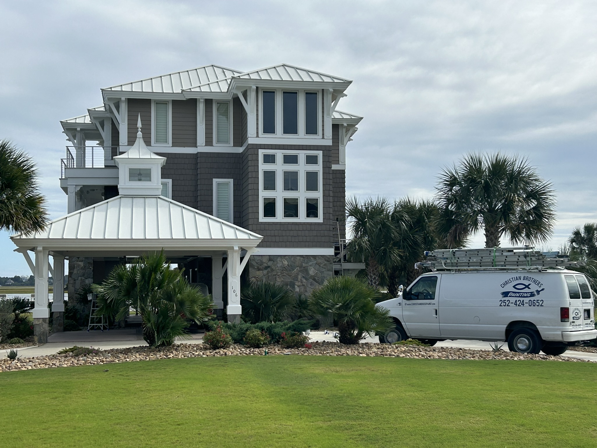 5B2AFE27-31ED-4342-A9D8-E2C93F3FD1E3_1_102_o A white van is parked outside a large beach house with palm trees and a well-kept lawn.