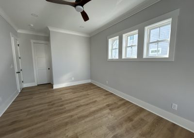 Empty room with light wood flooring, gray walls, three windows, and a ceiling fan.