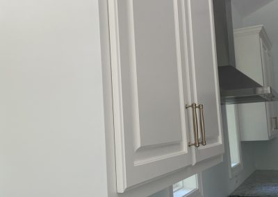 White kitchen cabinets with gold handles above a granite countertop and stove, near windows and outlets.