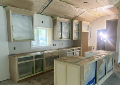 Kitchen under renovation with cabinets and ceiling covered in protective plastic, and construction lights set up.