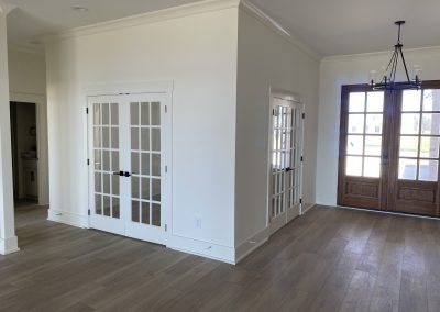 Bright room with wood floors, white walls, French doors, and large windows with double wooden doors.