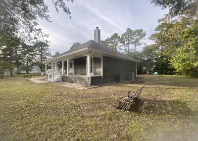Single-story house with a covered porch, surrounded by trees and a rake on the grass in the yard.
