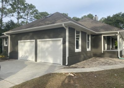A house with two white garage doors, gray siding, and a driveway on a sunny day.