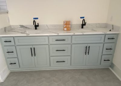 Light blue double-sink vanity with black fixtures, marble countertop, and hexagonal floor tiles.