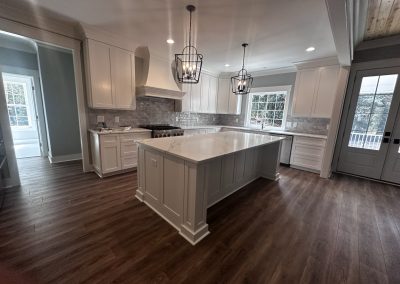 Modern kitchen with white cabinets, a large island, pendant lights, wood floors, and large windows.