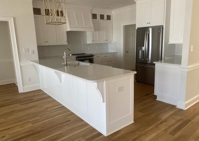 Modern kitchen with white cabinets, a large island, stainless steel fridge, and light wood flooring.