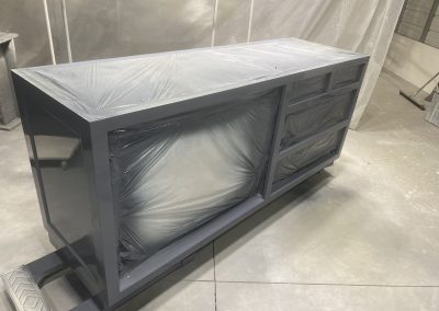 A freshly painted cabinet with plastic covering the drawers and shelves, in a workshop.