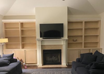 Living room with empty built-in shelves, a TV above a fireplace, two couches, and a child’s toy on the floor.
