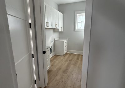 A small room with white cabinets, a desk, wood flooring, and a window letting in natural light.