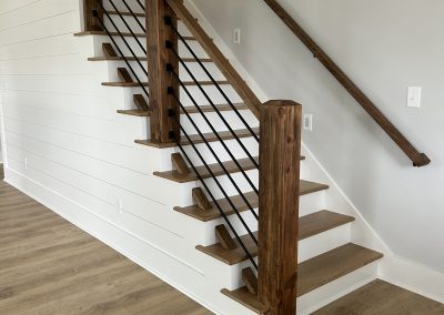 Modern wooden staircase with metal railings and light brown steps against a white shiplap wall.