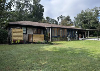 Single-story house with a covered porch, wooden fence panels, and ladders in the front yard.