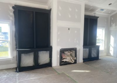 Living room under renovation with covered fireplace and built-in shelves, walls partially painted.