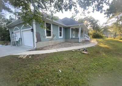 A green house with white trim, a front porch, and a curved sidewalk on a grassy yard.