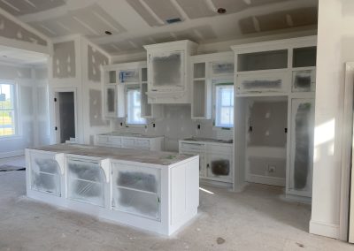 A kitchen under construction with white cabinets, plastic coverings, and unfinished walls and floors.