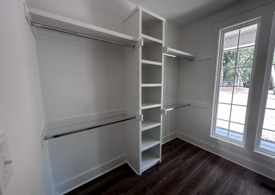Empty walk-in closet with white shelves, hanging rods, and a large window letting in natural light.
