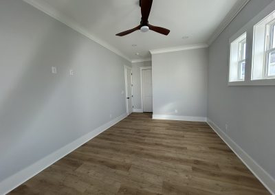 Empty room with light gray walls, wood floor, ceiling fan, and three small windows on the right.